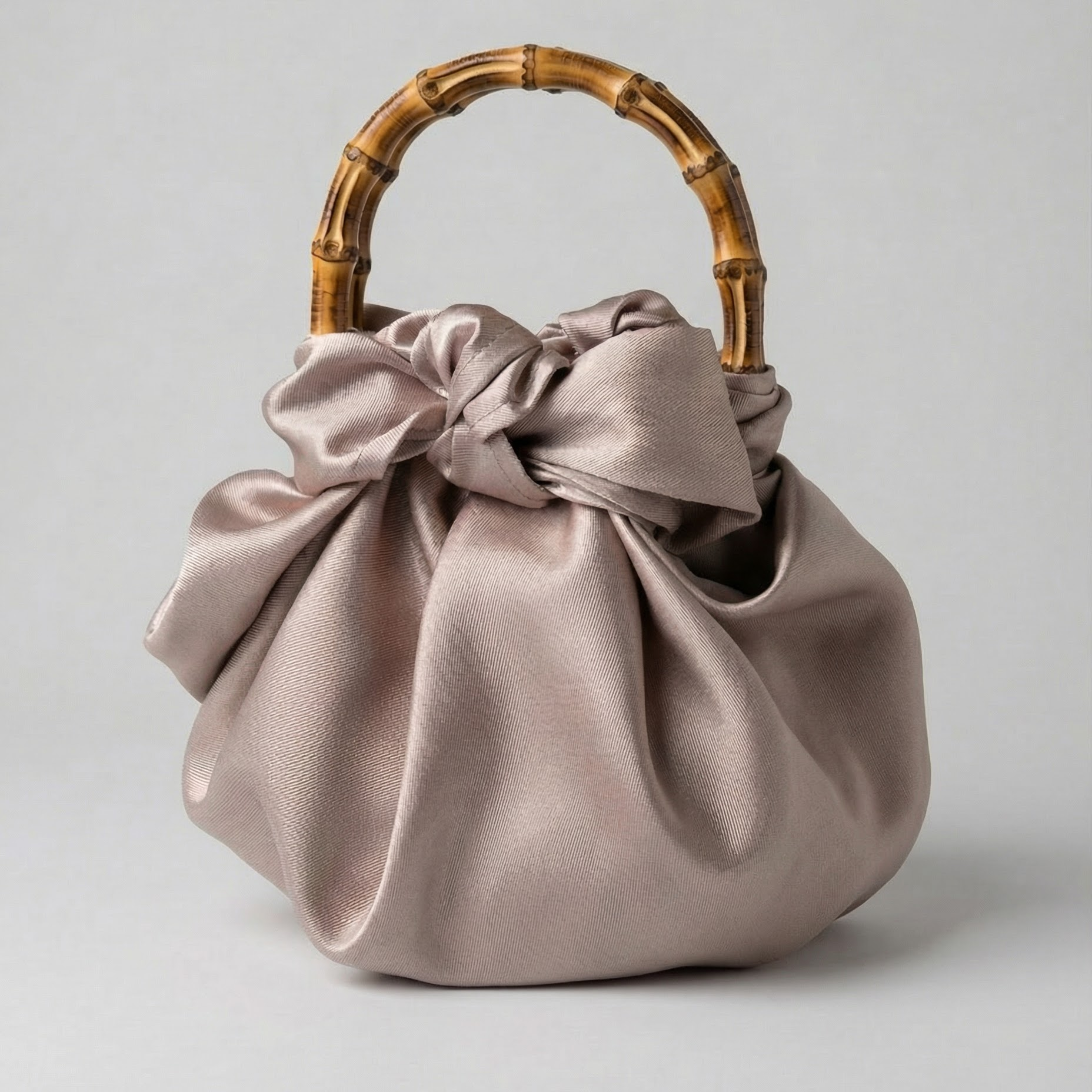 Satin dusty rose handbag with a bamboo handle on a light gray background