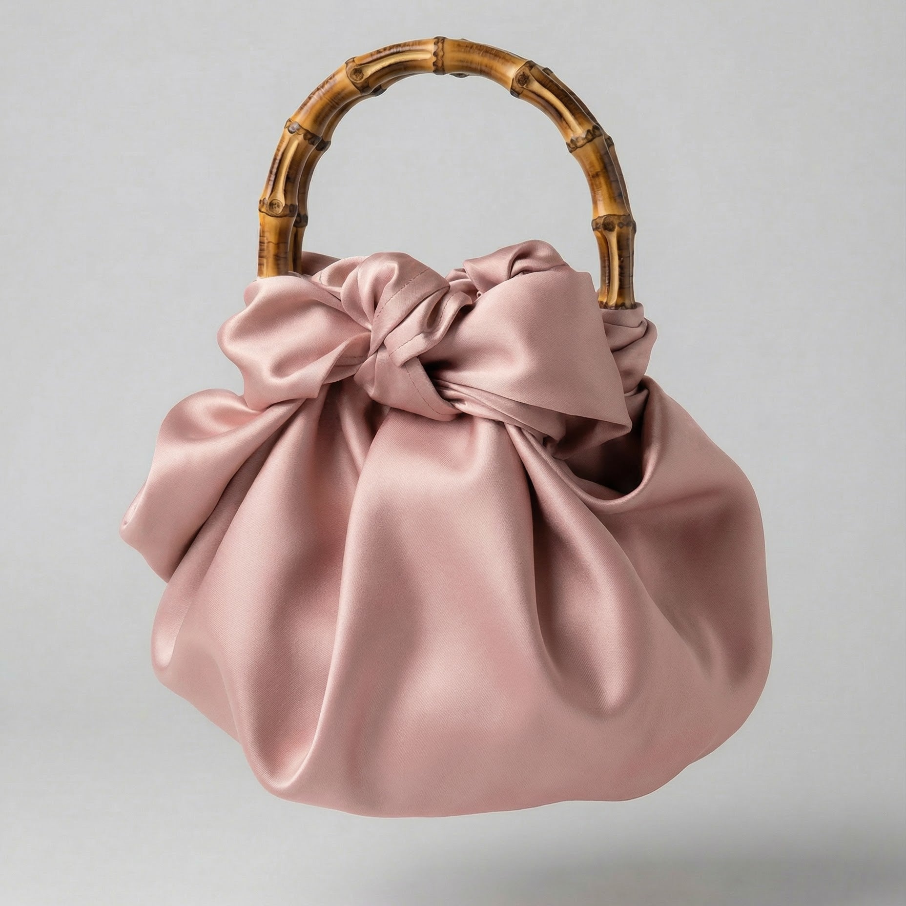 Pink satin handbag with a bamboo handle on a light gray background