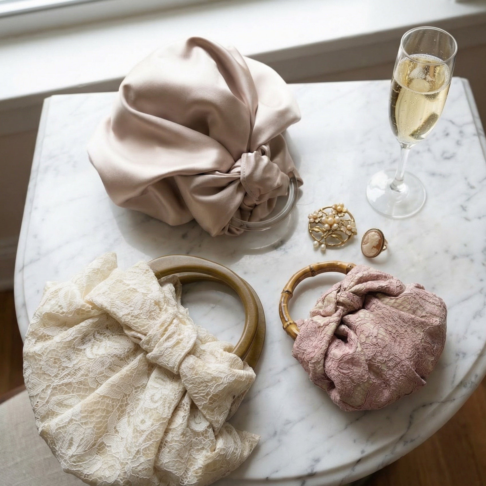 Three knotted fabric pochette bags by for keeps on a marble surface with a glass of champagne.