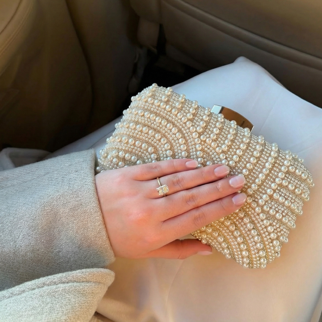 Hand holding a pearl embellished clutch in a car.