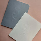 Two notebooks with embossed logo on a pink background