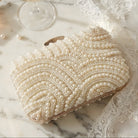 Pearl clutch bridal bag on a marble surface with a glass of champagne and a perfume bottle.