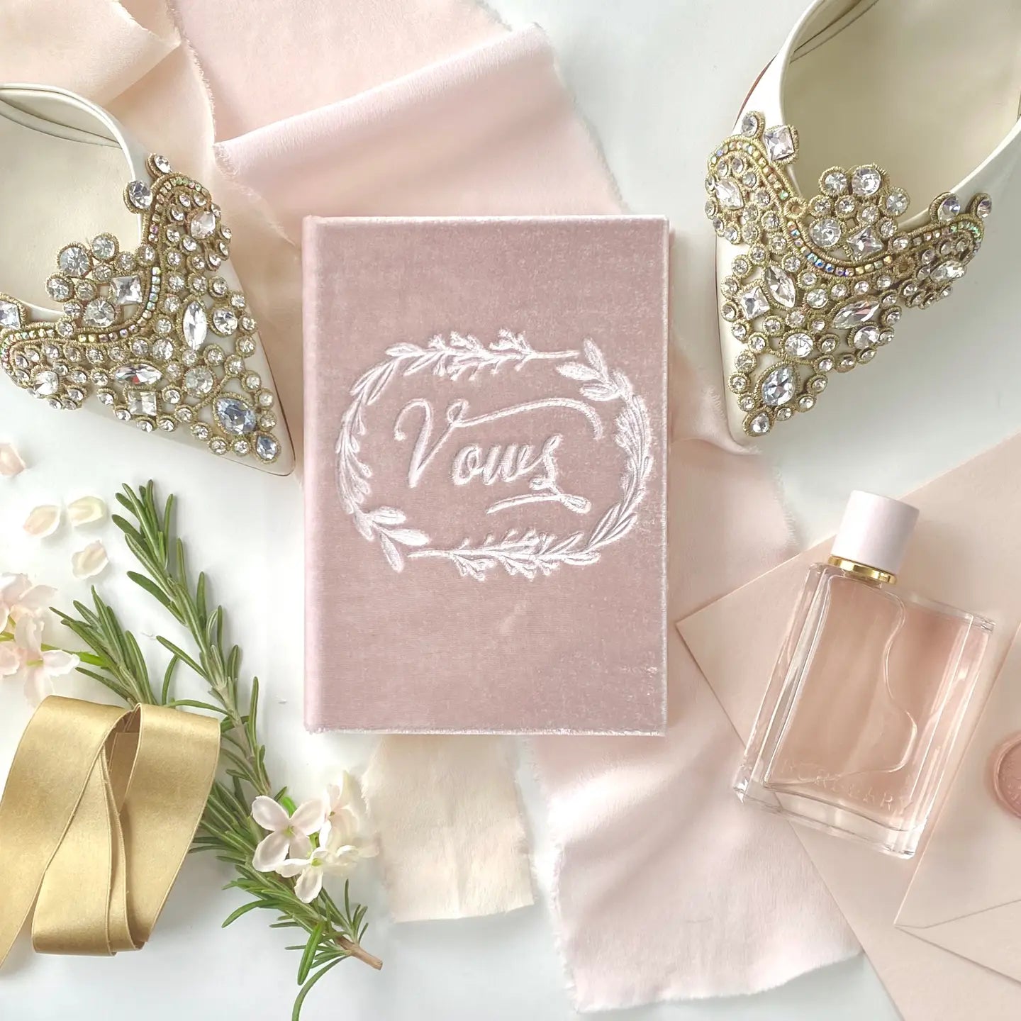 Pink 'Vows' book with decorative jewelry and flowers on a light background