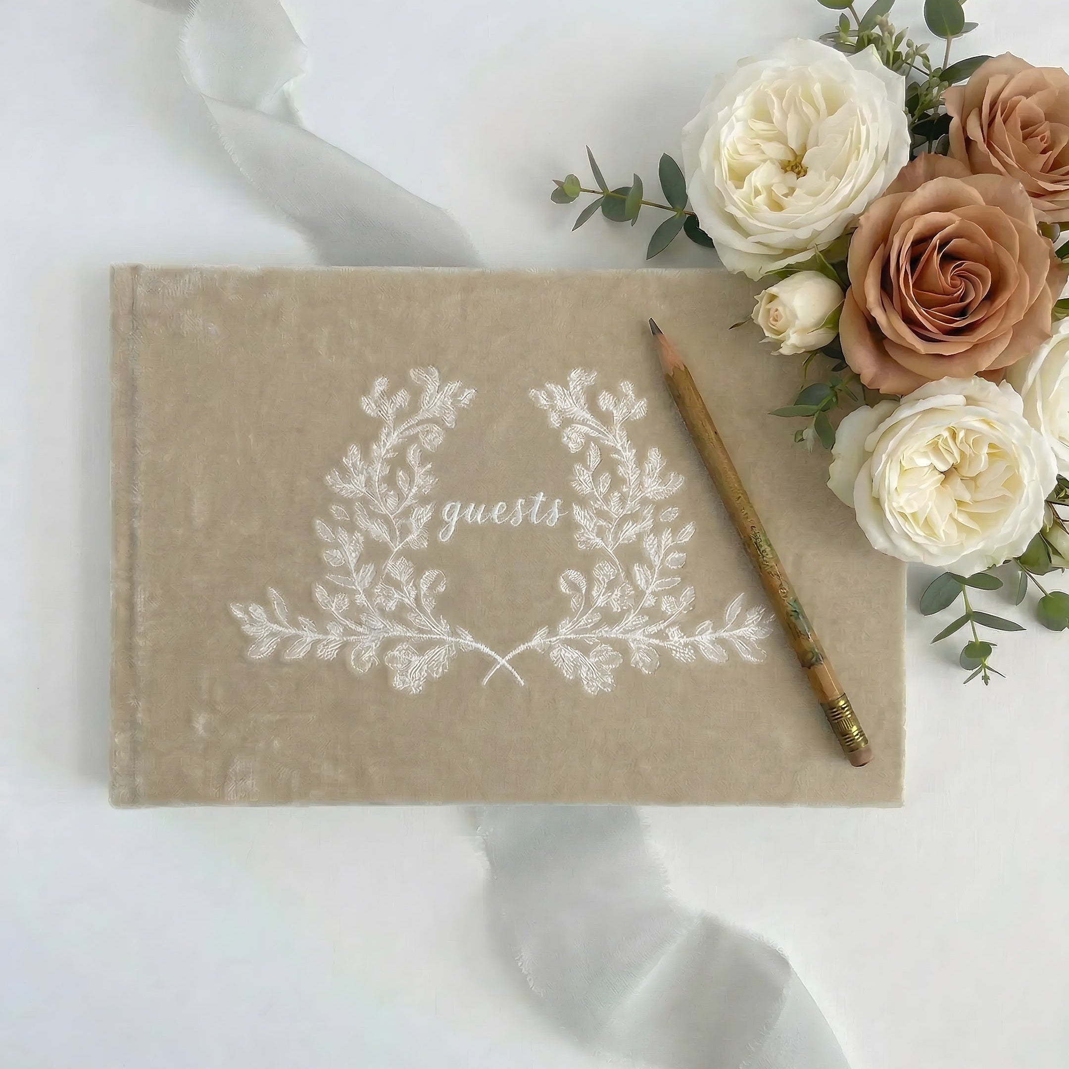 Guestbook with floral design and pencil on a white surface with flowers.