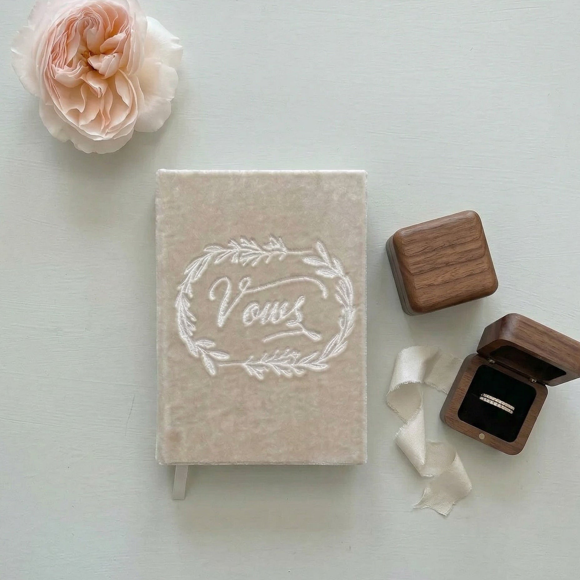 Book titled 'Vows' with a wooden ring box and pink rose on a light background