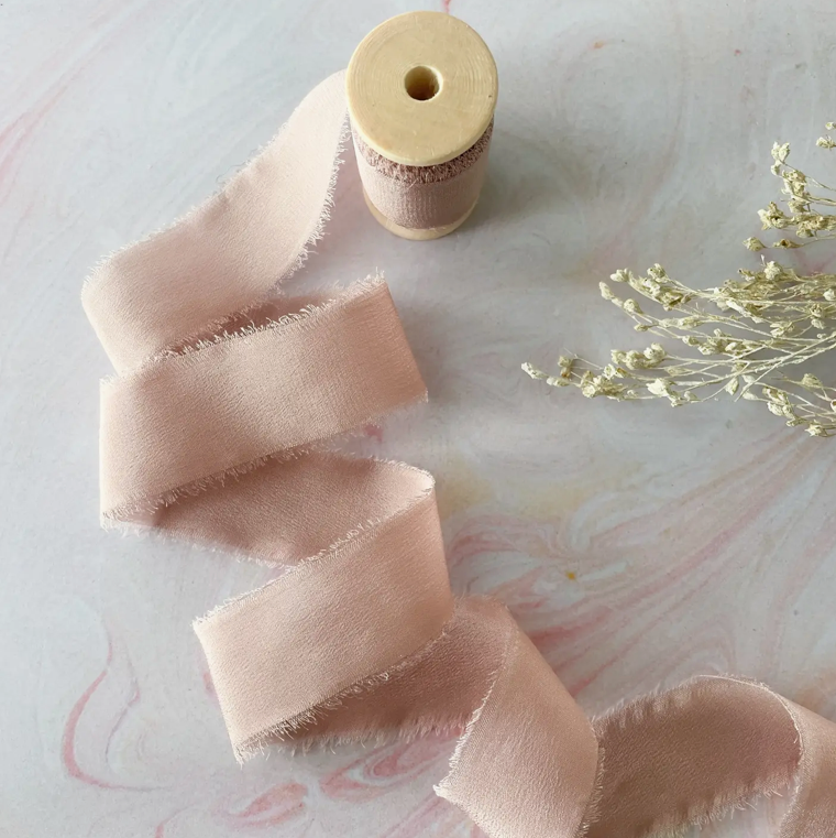 Blush pink ribbon with a wooden spool on a marble surface