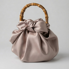 Satin dusty rose handbag with a bamboo handle on a light gray background