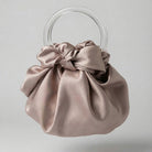 Dusty Rose satin handbag with clear circular handles on a light gray background