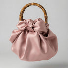 Pink satin handbag with a bamboo handle on a light gray background