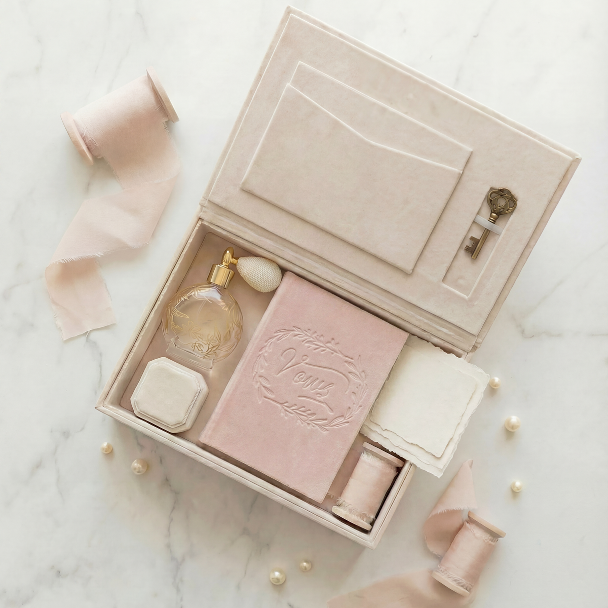 The EVR Heirloom wedding keepsake box covered in ivory linen, and filled with a perfume bottle, ring box, velvet vow book and ribbon spool