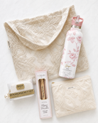 Collection of beauty products including a Boujee Bottle water bottle, bling ring cleaning brush, and bridal emergency kit on a heirloom lace tote.