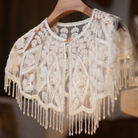 Lace shrug with fringe details on a wooden hanger against a blurred background