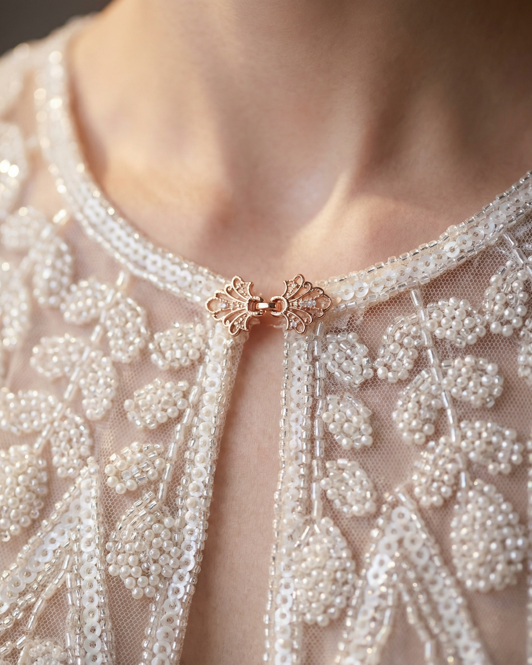 Close-up of a person wearing a delicate necklace with a rose gold clasp on an embroidered garment.