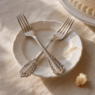 Two silver forks on a white plate with a cake in the background