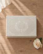 The EVR Box: a linen wedding keepsake box with hanji lace scrollwork on the lid, on a wooden table beside a white rose