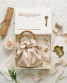 champagne mikado satin petite pochette in a linen wedding keepsake box with decorative elements and a marriage license scroll on a marble surface