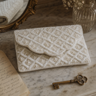 The For Keeps beaded scalloped clutch on a marble surface with brass skeleton key