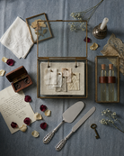 Decorative wedding flat laywith jewelry box, glass display cases, and vintage items on a textured surface.