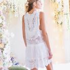 Bride wearing a white lace dress against a floral backdrop