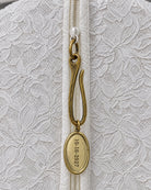 Brass wedding date charm on garment bag zipper: an antique brass hook and oval medallion hand-stamped 10-10-2027 on the ivory lace bridal garment bag