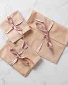 Three beige gift bags with pink ribbons on a marble surface