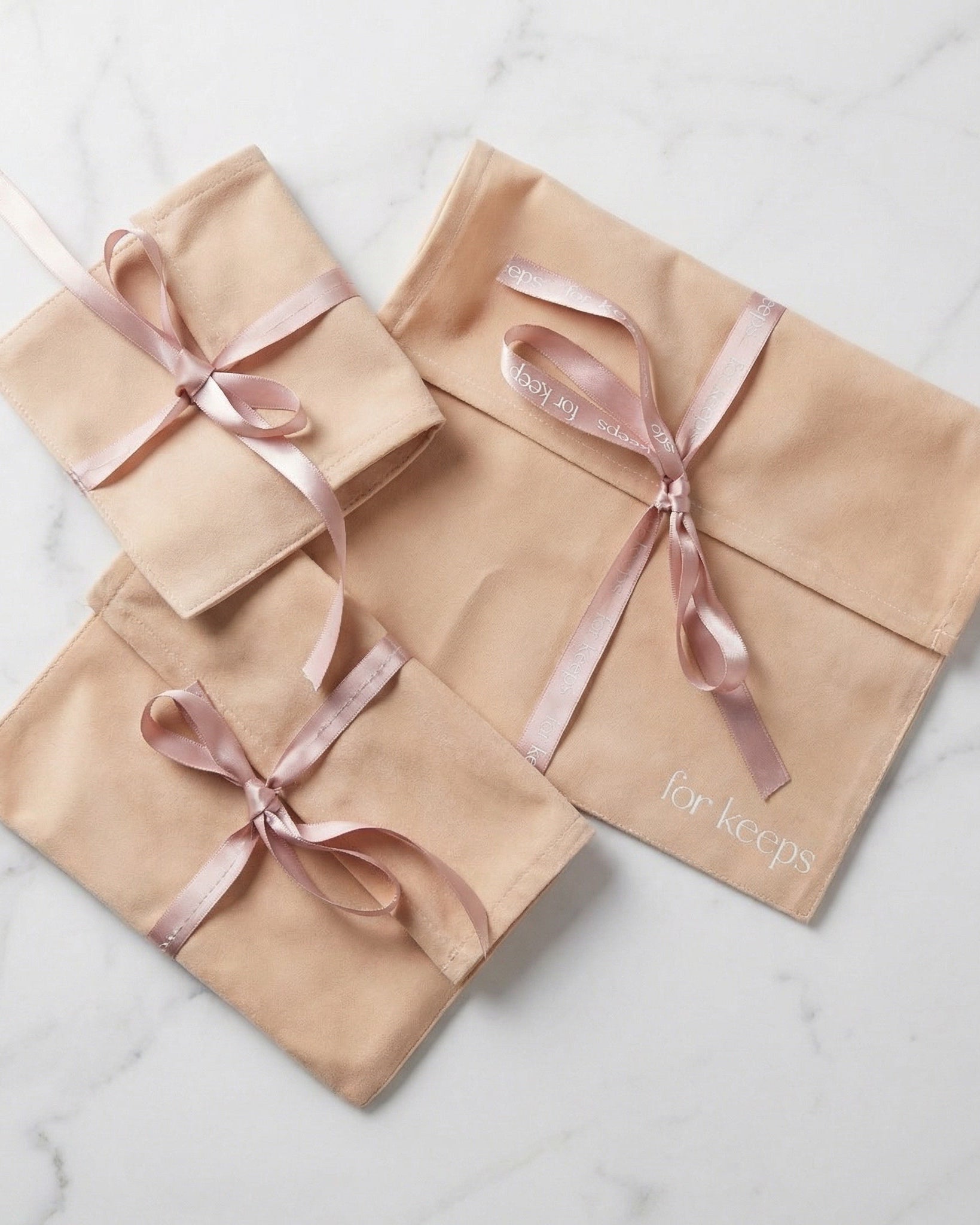 Three beige gift bags with pink ribbons on a marble surface